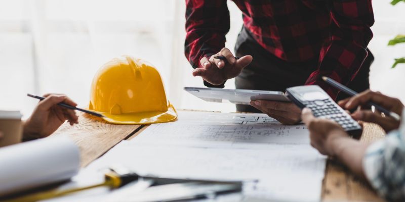 Construction team reviewing blueprints and calculations at a table with a yellow hard hat.