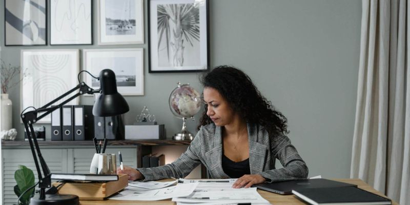 Woman in a gray suit working at a desk with papers and lamp in a stylish home office.