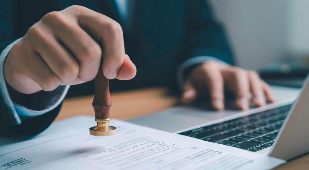 a man in a suit is using a laptop and placing a stamp on a document