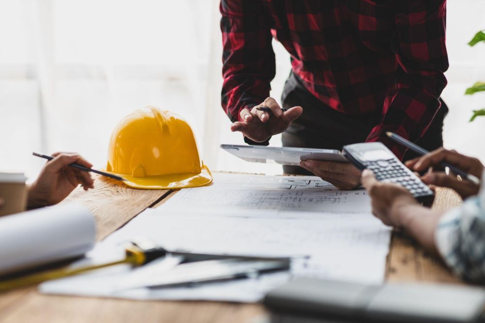 Construction team reviewing blueprints and calculations at a table with a yellow hard hat.