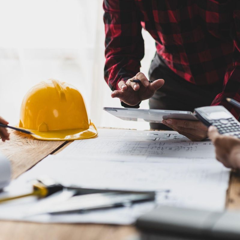 Construction team reviewing blueprints and calculations at a table with a yellow hard hat.