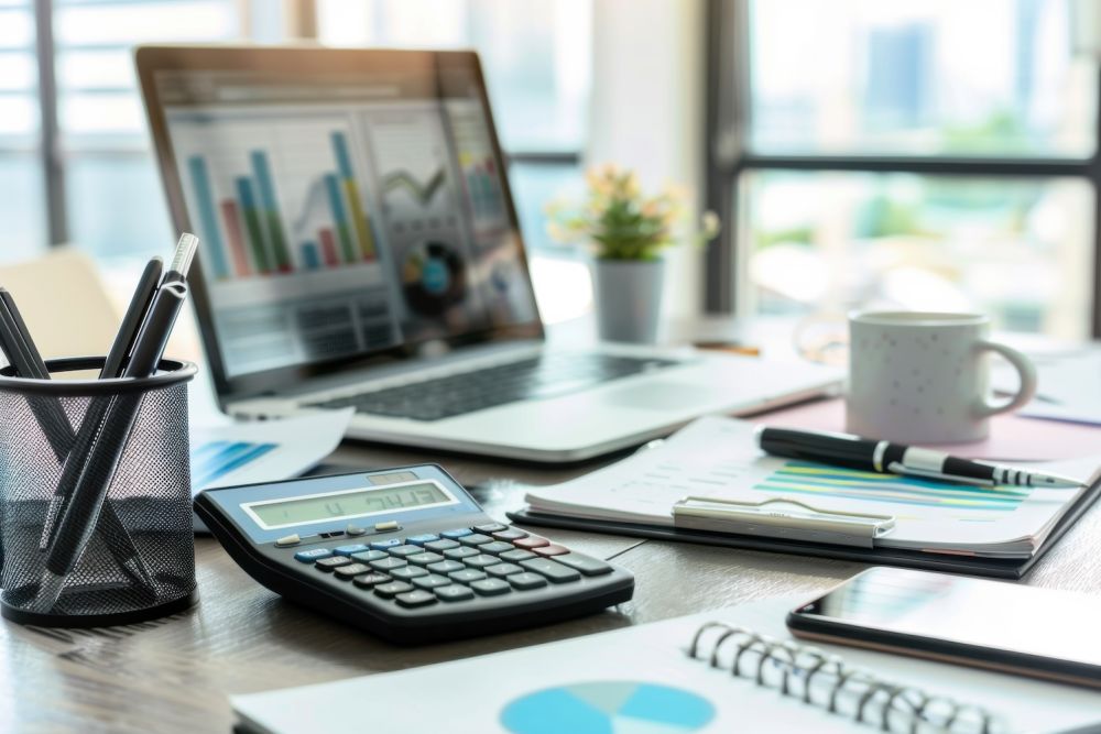 Office desk with laptop, graphs, calculator, and coffee mug, displaying financial analysis and planning tools.