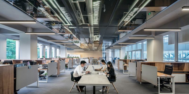 Modern open-plan office with minimalist design, employees working at a shared table under sleek lighting.